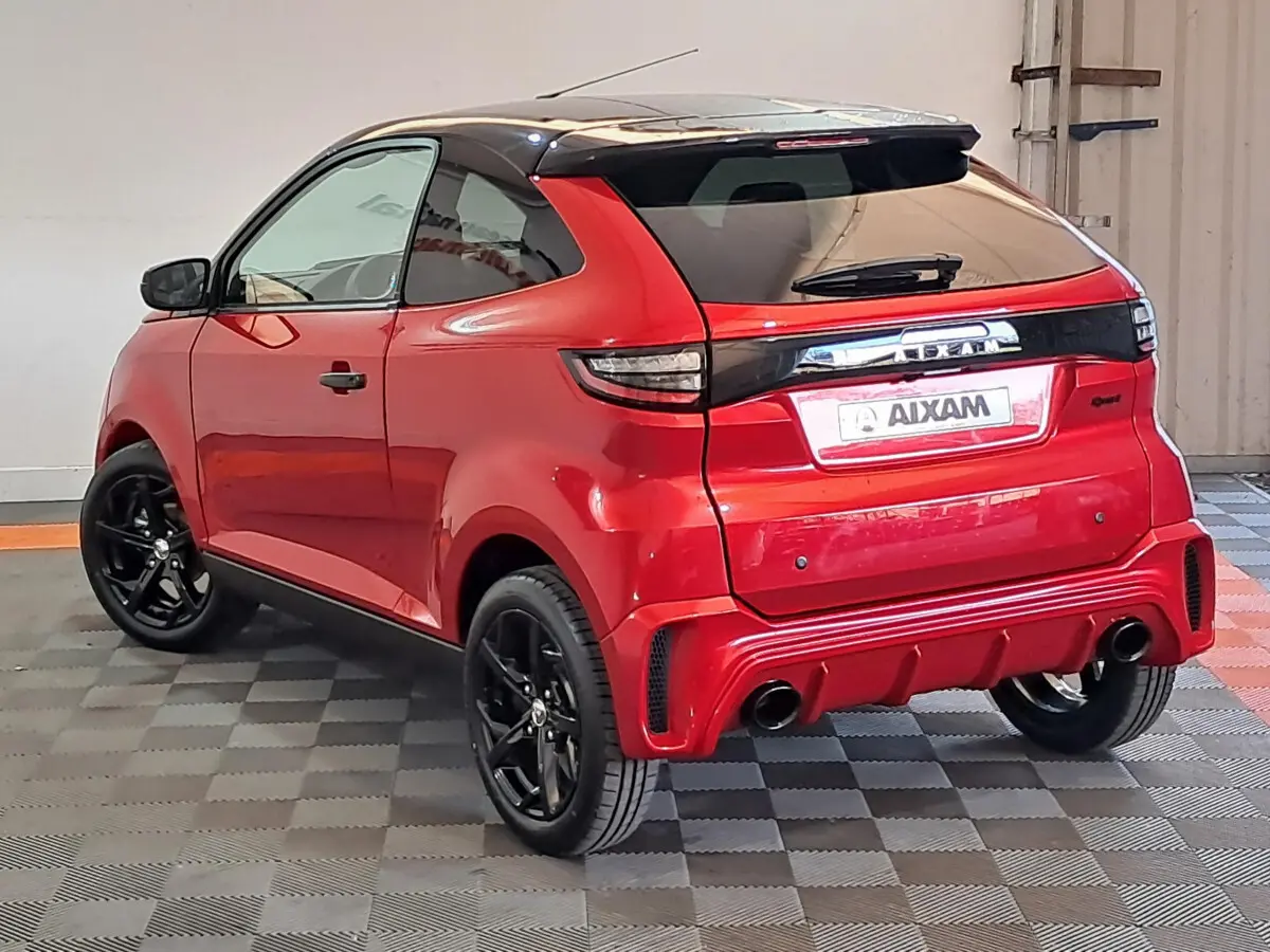 Vue 3/4 arrière droite d'une Aixam Ambition rouge avec jantes noires et toit noir brillant dans un garage.