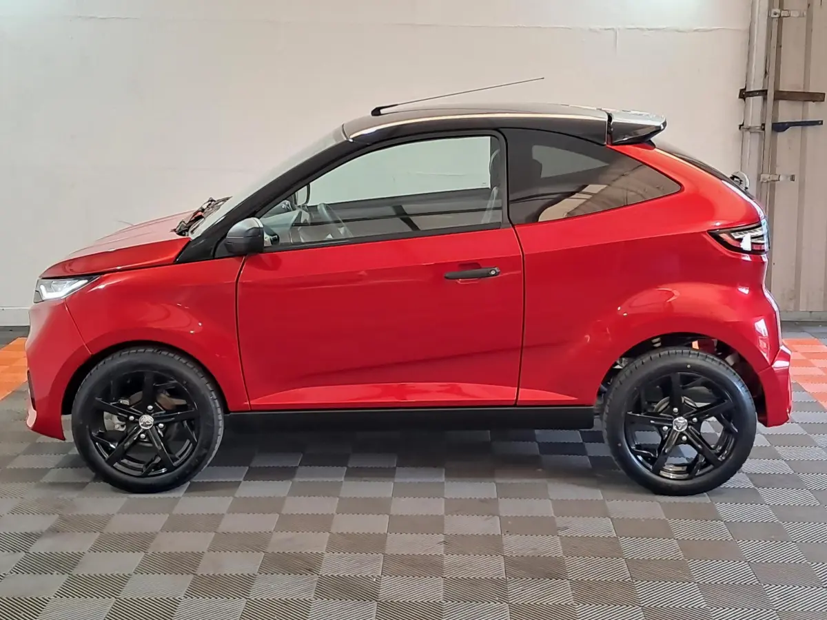 Vue de profil côté gauche d'une Aixam Ambition rouge 2025 avec jantes noires et toit noir contrasté.