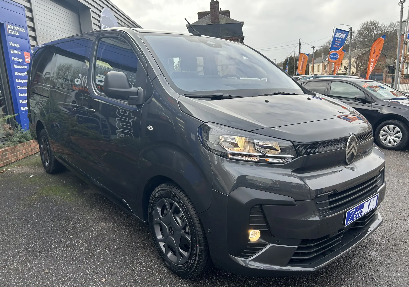 Vue 3/4 avant gauche d'un Citroën Jumpy Cabine Approfondie gris titane métal avec phares allumés sur parking.