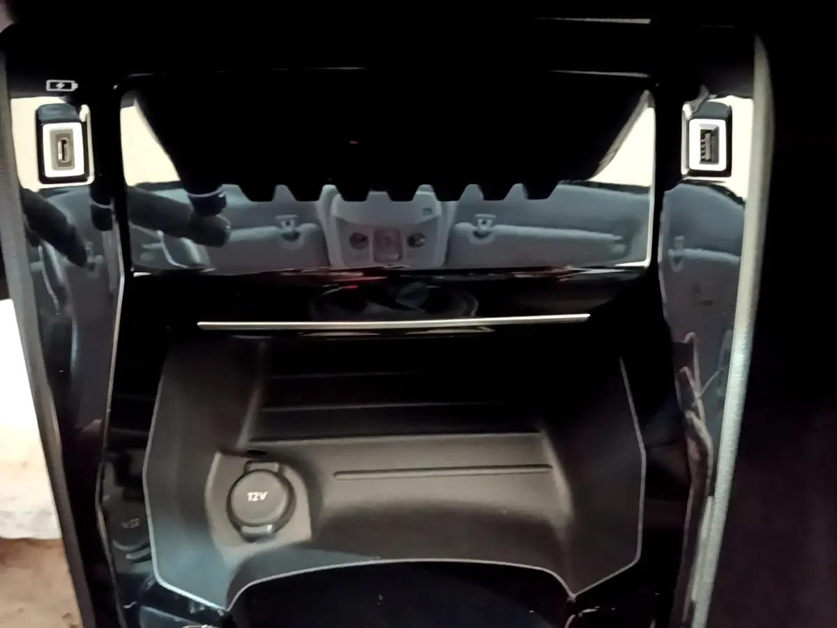 Vue rapprochée de la console centrale noire avec prise 12V et ports USB de la Peugeot 208 blanche 2021.