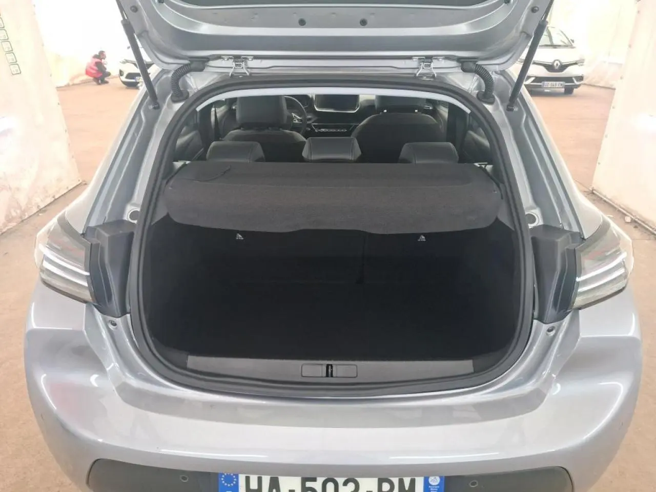 Vue arrière ouverte sur le coffre d'une Peugeot 208 gris clair 2024, mettant en valeur l'espace de chargement et les feux arrière.