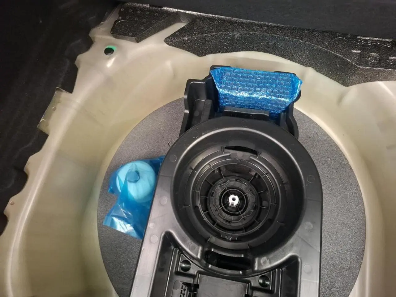 Vue plongeante sur le coffre d’un Peugeot 208 gris clair 2024, montrant le logement de la roue de secours et ses accessoires.