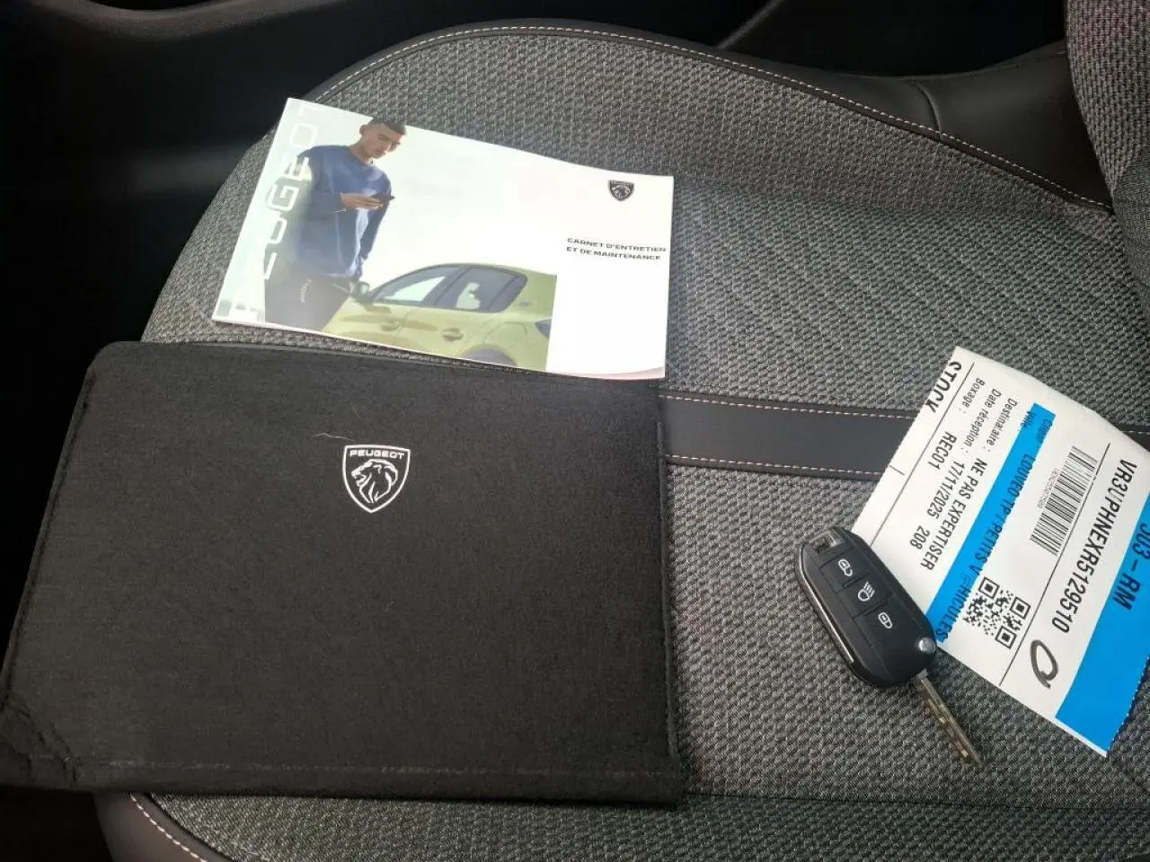 Clé de voiture Peugeot 208 posée sur un siège gris clair avec manuel d'entretien et pochette noire Peugeot.