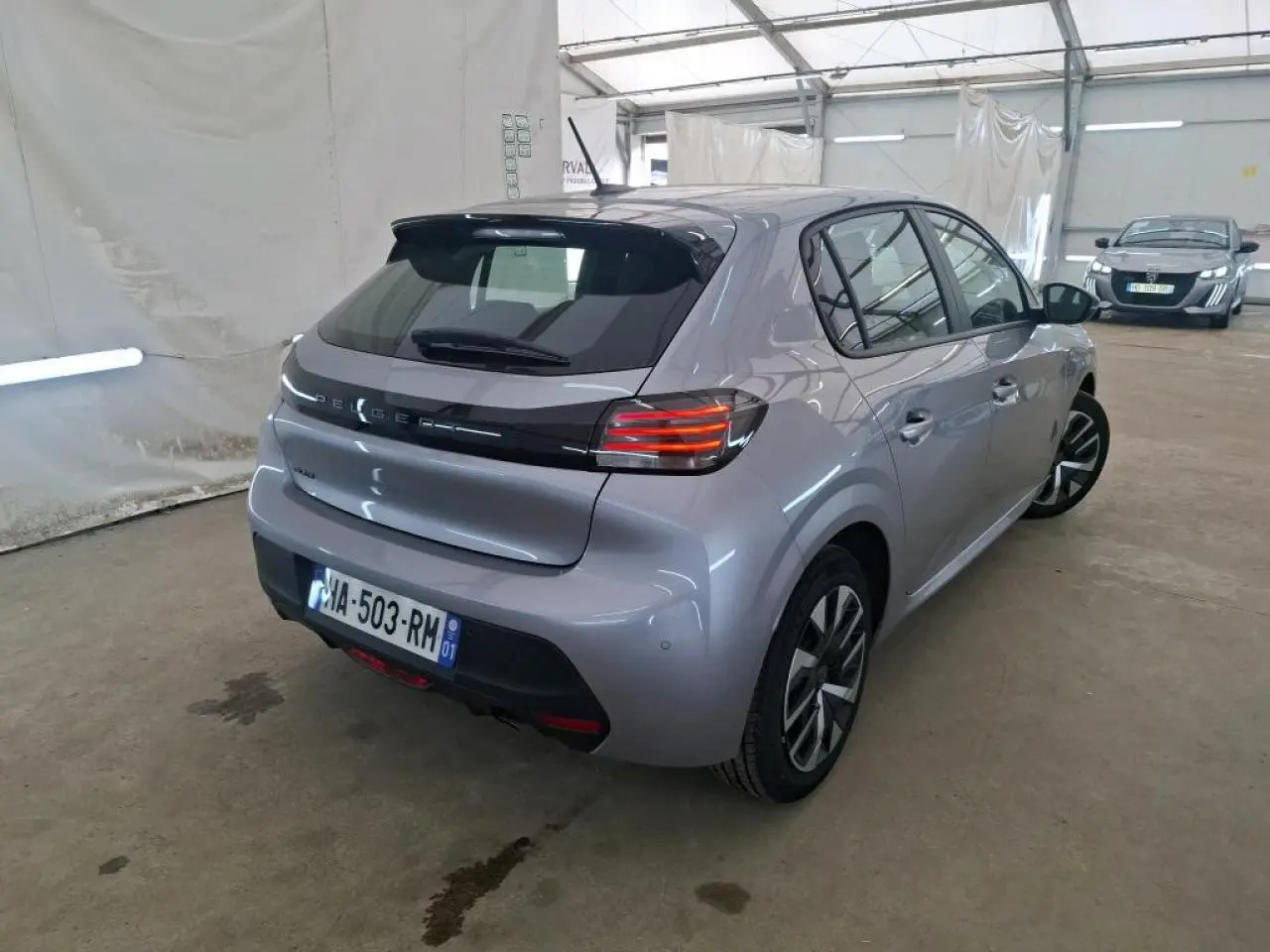 Vue 3/4 arrière droit d'une Peugeot 208 gris clair 2024 avec feux arrière LED et jantes alliage bicolores.