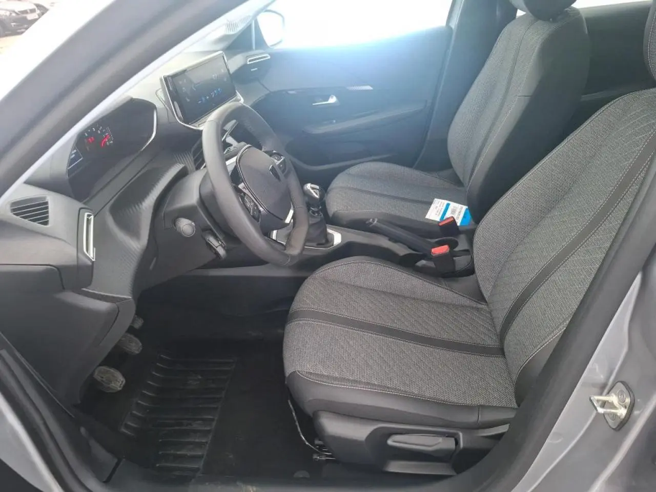 Intérieur avant droit de la Peugeot 208 gris clair 2024, montrant les sièges tissu, volant compact et boîte manuelle.