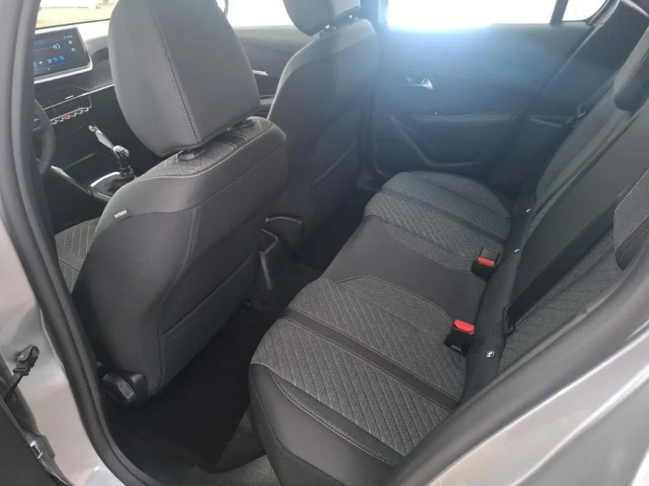 Vue intérieure arrière côté gauche de la Peugeot 208 2024 gris clair, montrant les sièges arrière et la console avant avec boîte manuelle.