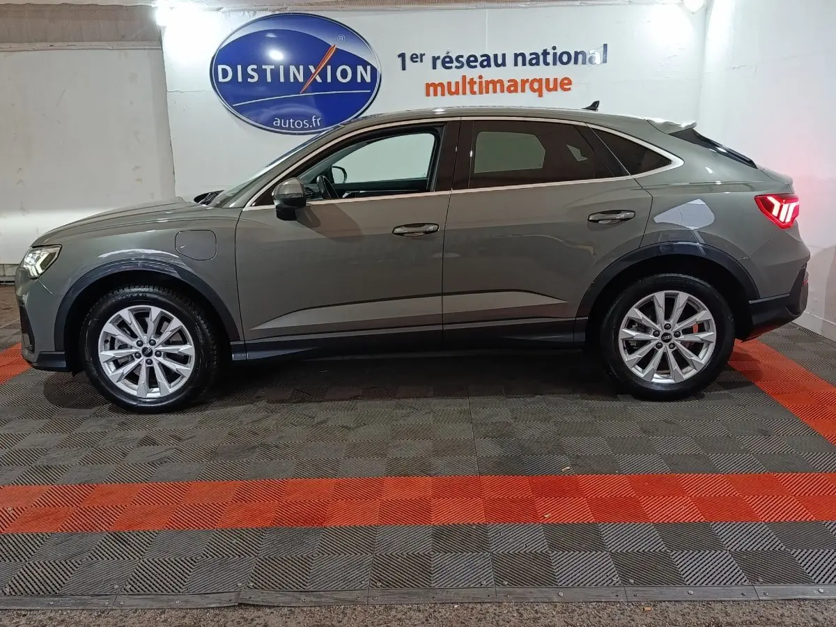 Audi Q3 Sportback gris foncé vue de profil côté gauche, avec jantes alliage et feux arrière allumés.