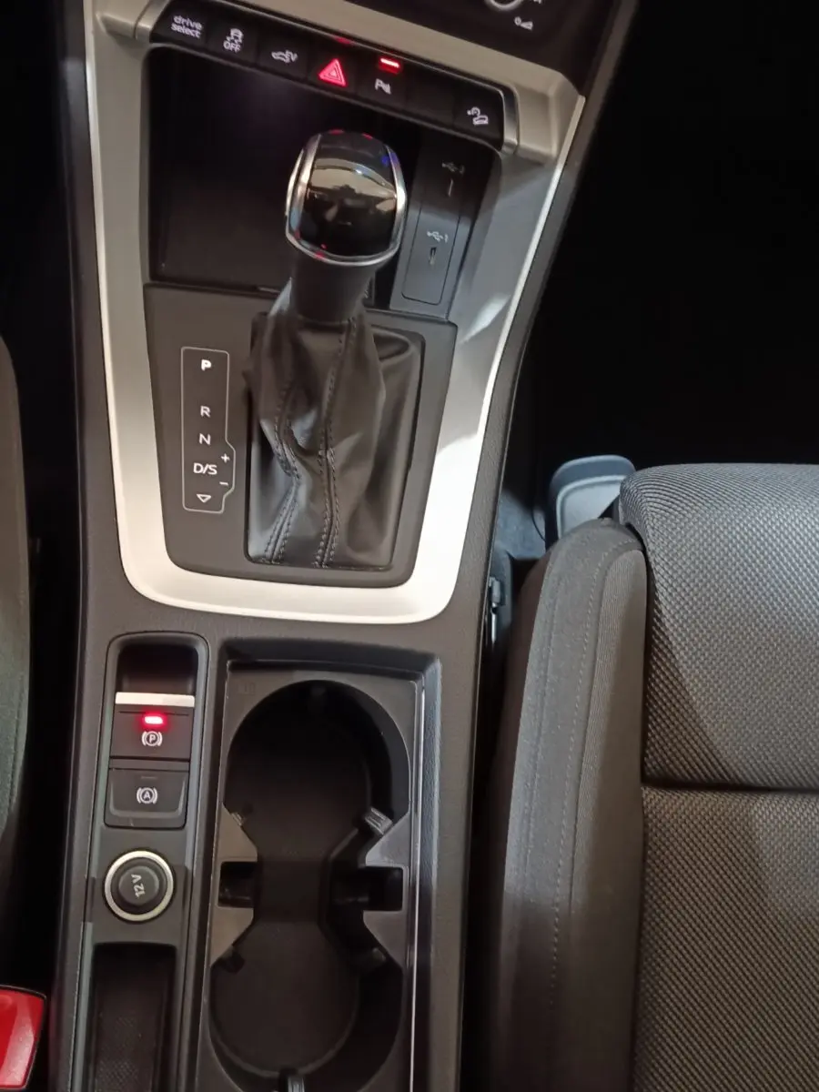 Vue rapprochée de la console centrale de l’Audi Q3 Sportback 45 TFSI e, avec levier de vitesse et porte-gobelets noirs.