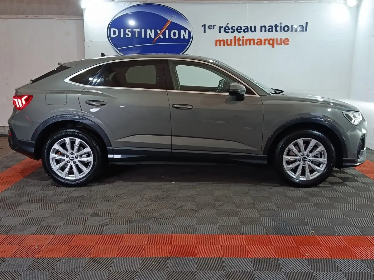 Profil droit d’un Audi Q3 Sportback gris foncé hybride rechargeable 2021, avec jantes alliage et feux arrière allumés.