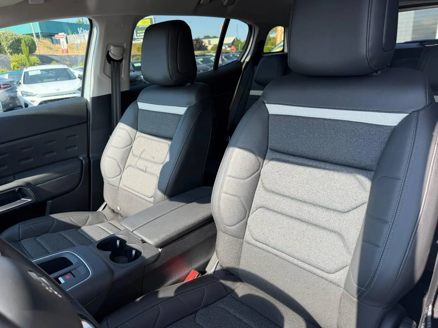Vue rapprochée des sièges avant en tissu noir et gris du Citroën C5 Aircross 2025, avec accoudoir central et porte-gobelets.