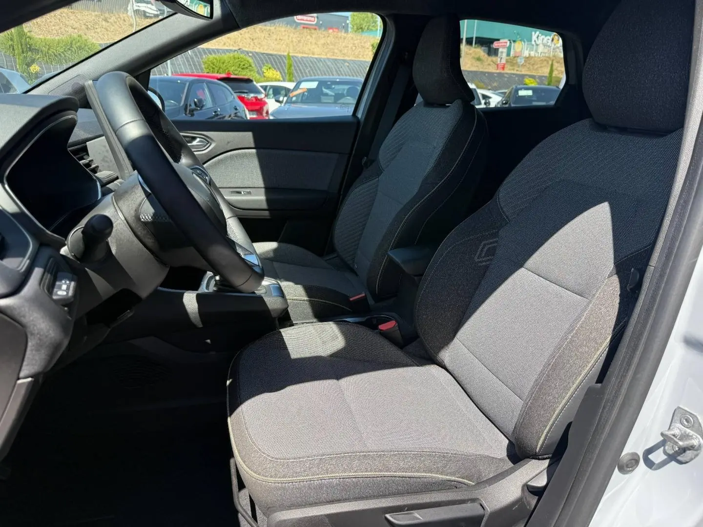 Vue intérieure côté conducteur du Renault Captur 2025, sièges gris avec accoudoir central et volant multifonction.