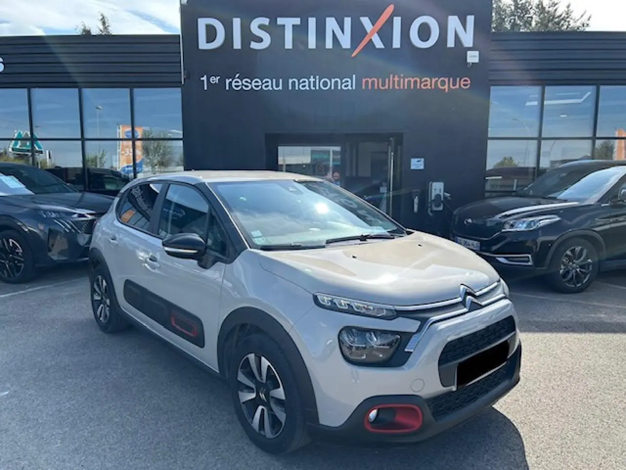 Citroën C3 sable métal vue 3/4 avant droit avec protections latérales noires et touches rouges sur pare-chocs.