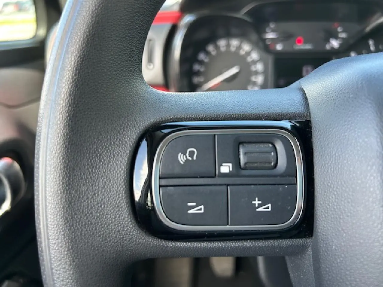 Gros plan sur les commandes audio au volant d'une Citroën C3 sable métal de 2021, intérieur noir.