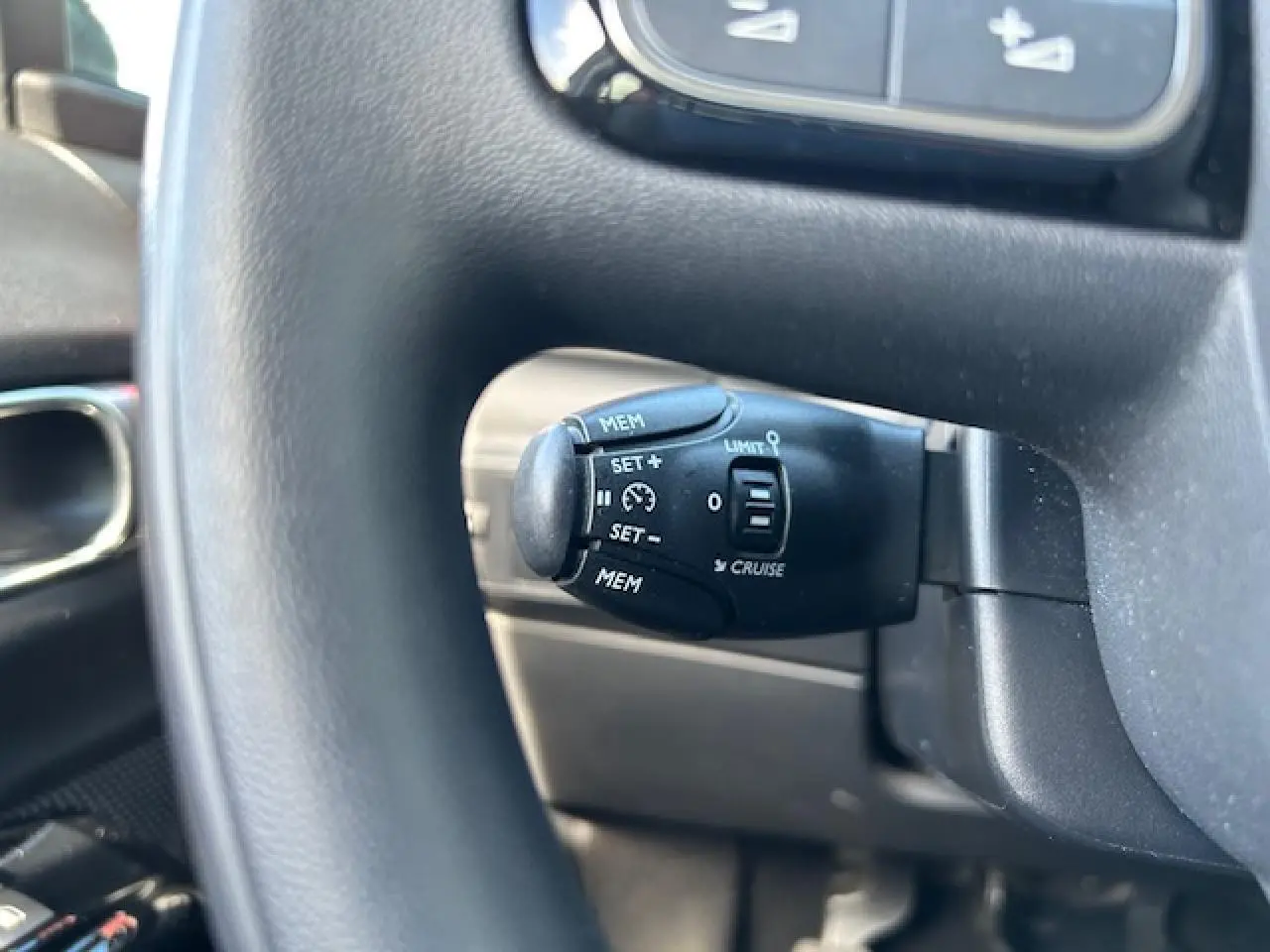 Gros plan sur la commande de régulateur de vitesse noire, située derrière le volant de la Citroën C3 sable métal.