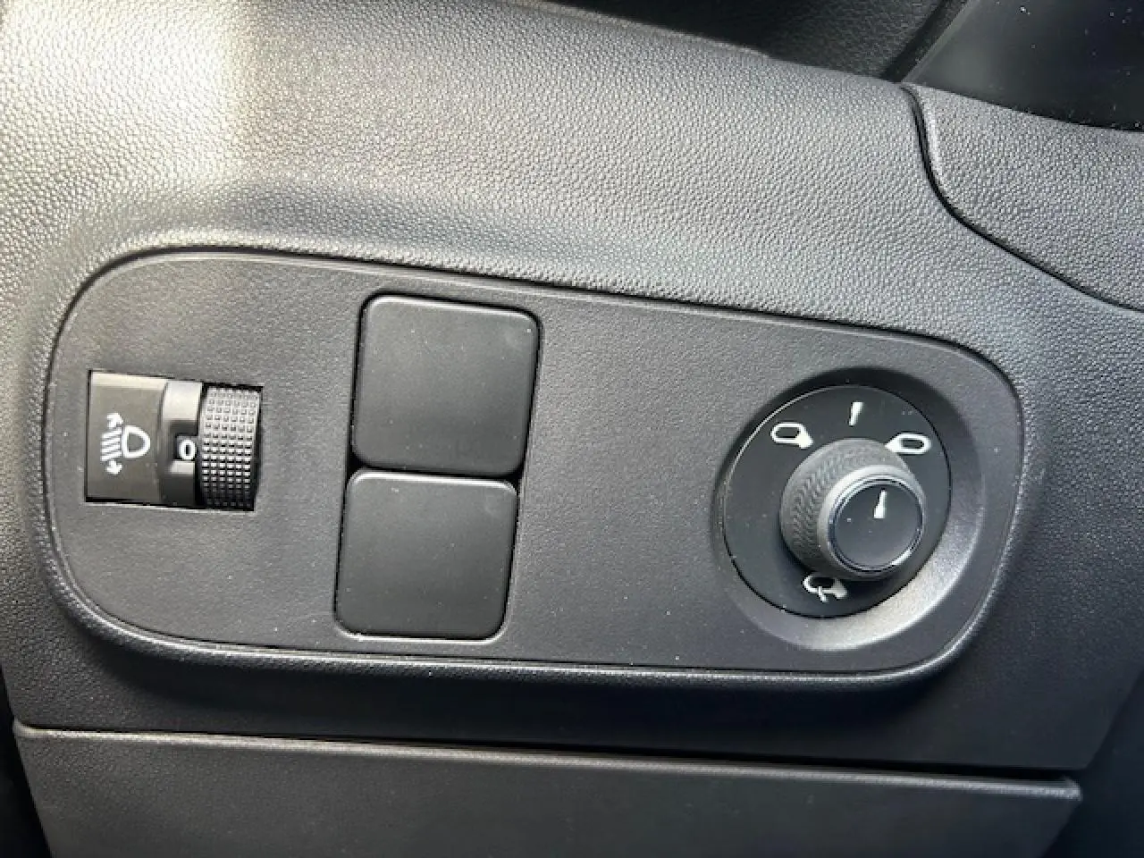 Gros plan sur les commandes noires de réglage des phares et des rétroviseurs dans une Citroën C3 sable métal de 2021.