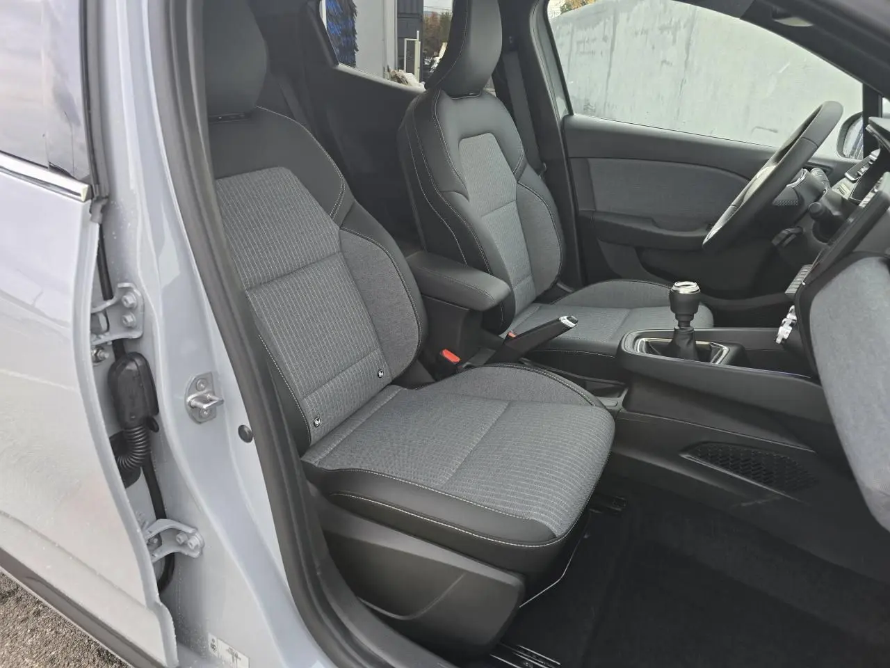 Vue intérieure côté gauche de la Renault Clio 2025 gris Rafale, sièges tissu gris avec coutures blanches et levier de vitesse manuel.