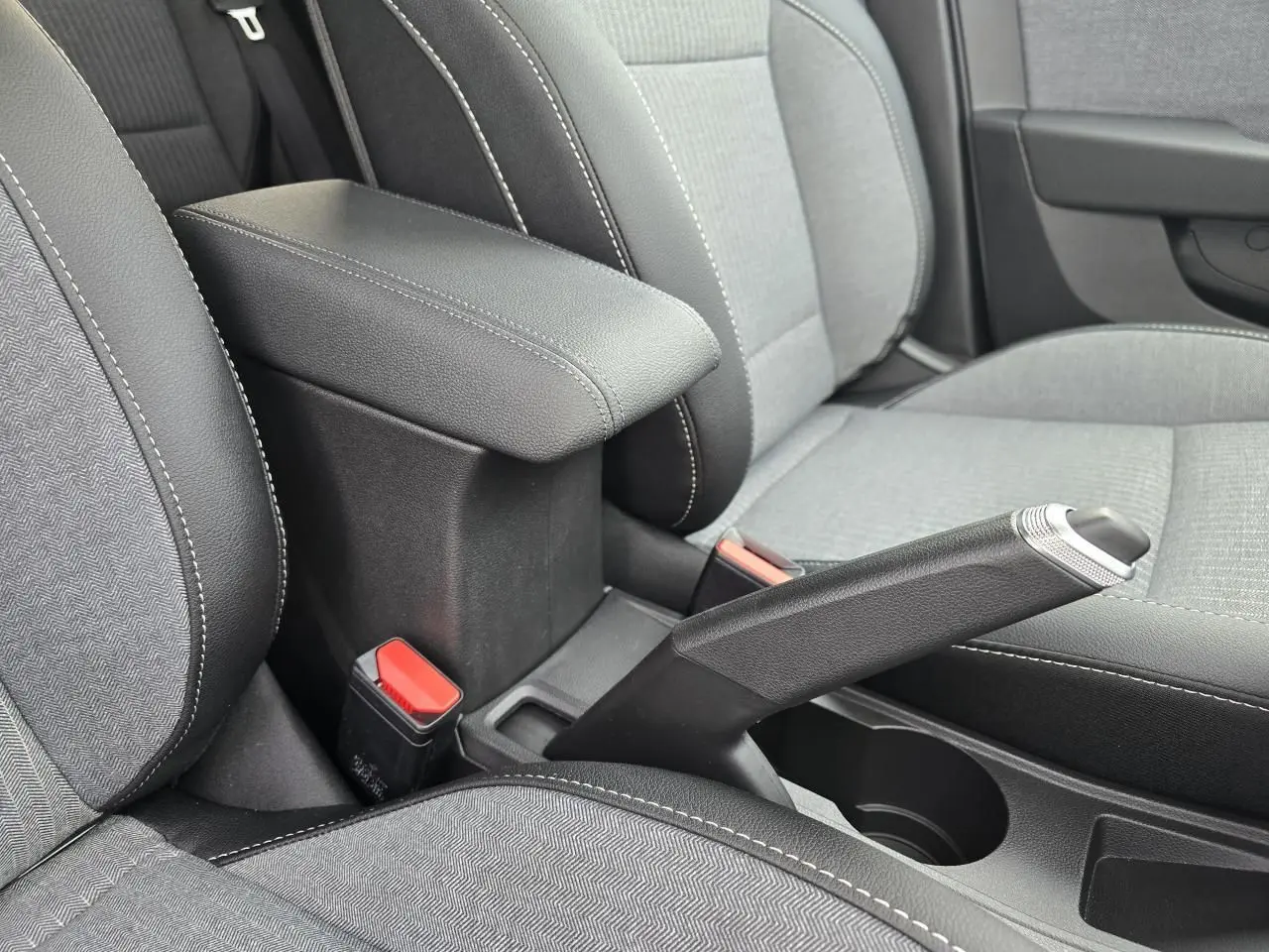 Vue rapprochée de l'accoudoir central coulissant et frein à main manuel entre les sièges gris clair et noir de la Renault Clio V.