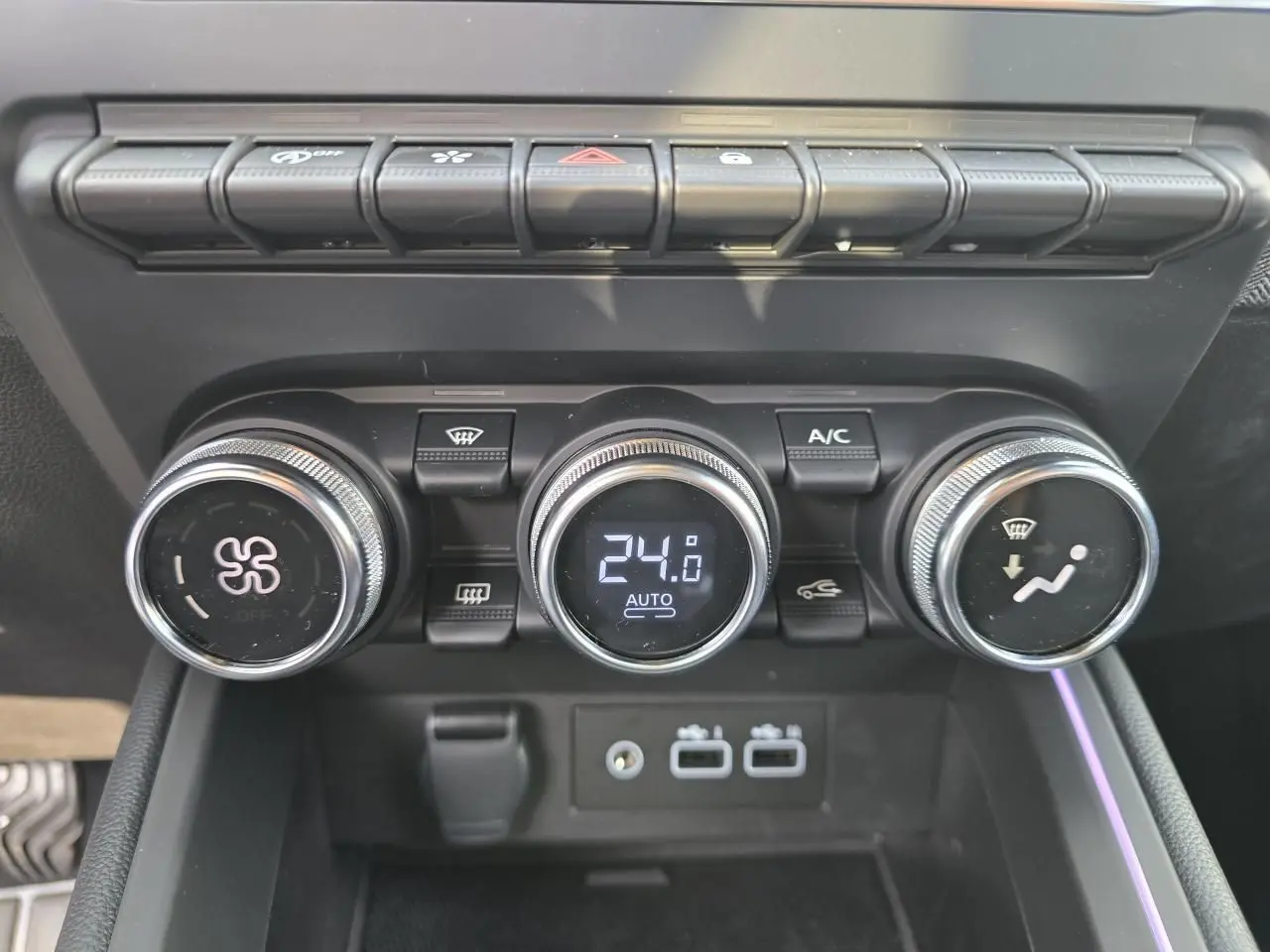 Gros plan sur la console centrale de la Renault Clio 2025, boutons de climatisation et ports USB visibles.