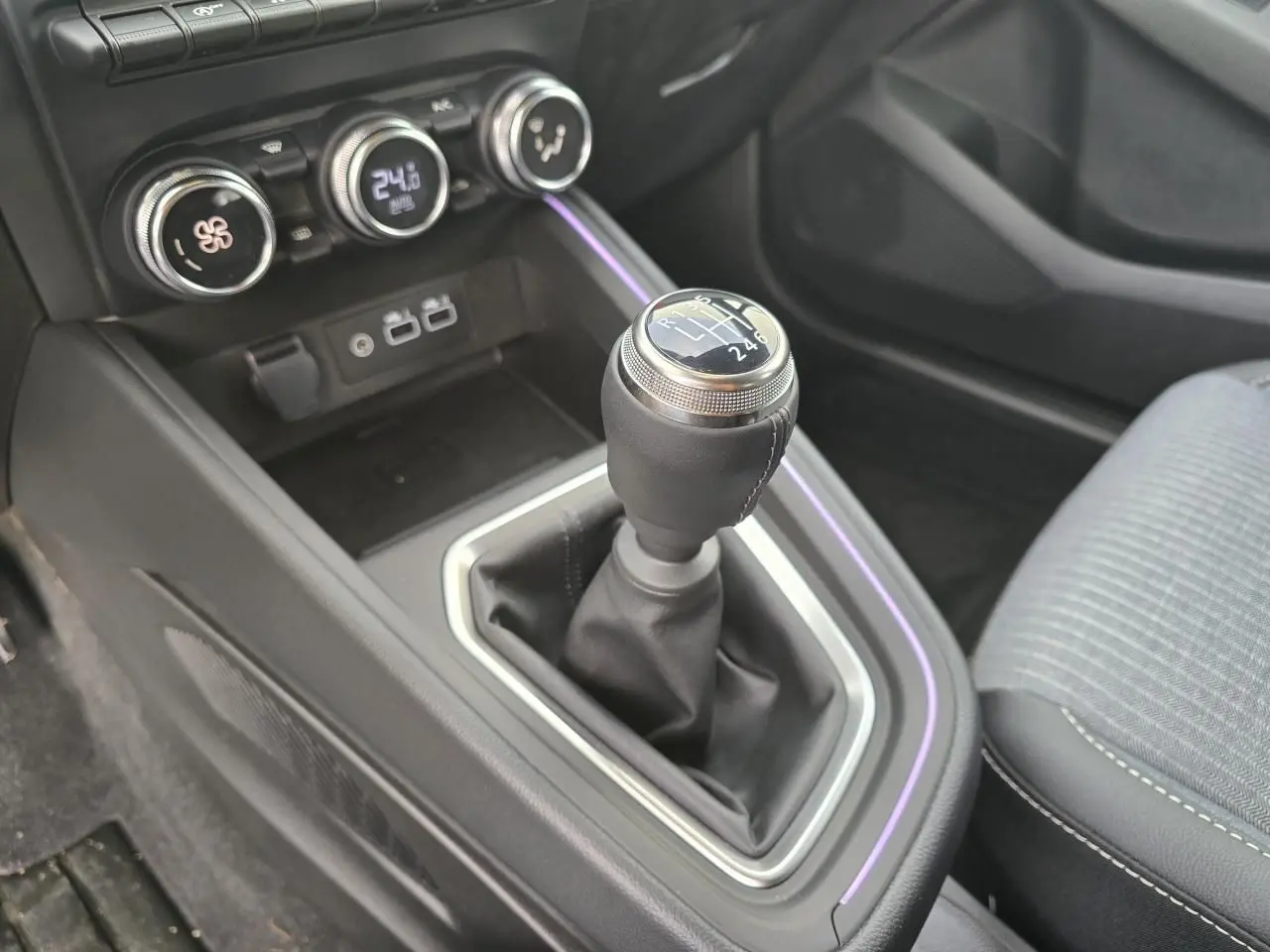 Gros plan sur la boîte manuelle et la console centrale noire avec éclairage d'ambiance violet dans une Renault Clio gris Rafale.