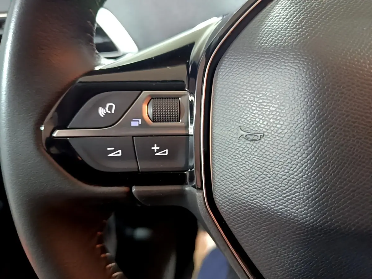 Gros plan sur le volant cuir noir du Peugeot 5008 2021, avec commandes multifonctions et bouton de volume.