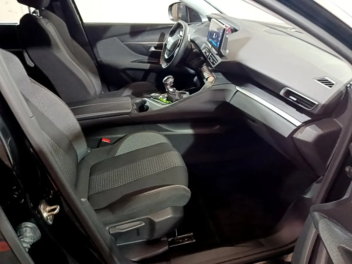 Vue intérieure côté passager avant du Peugeot 5008 noir 2021, montrant sièges tissu et tableau de bord avec écran tactile.