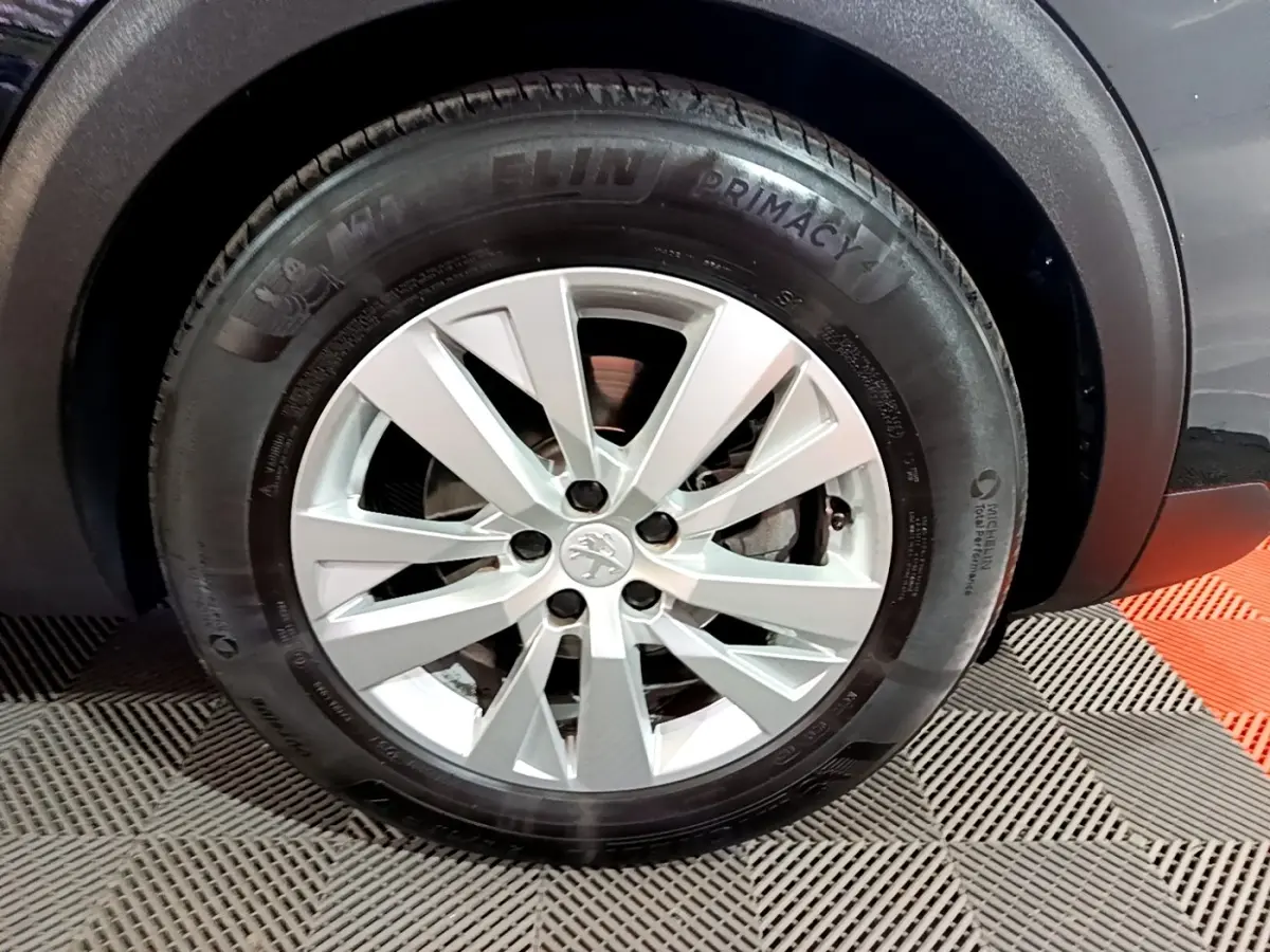 Gros plan sur la roue avant droite d’un Peugeot 5008 noir, mettant en valeur la jante argentée et le pneu Michelin.