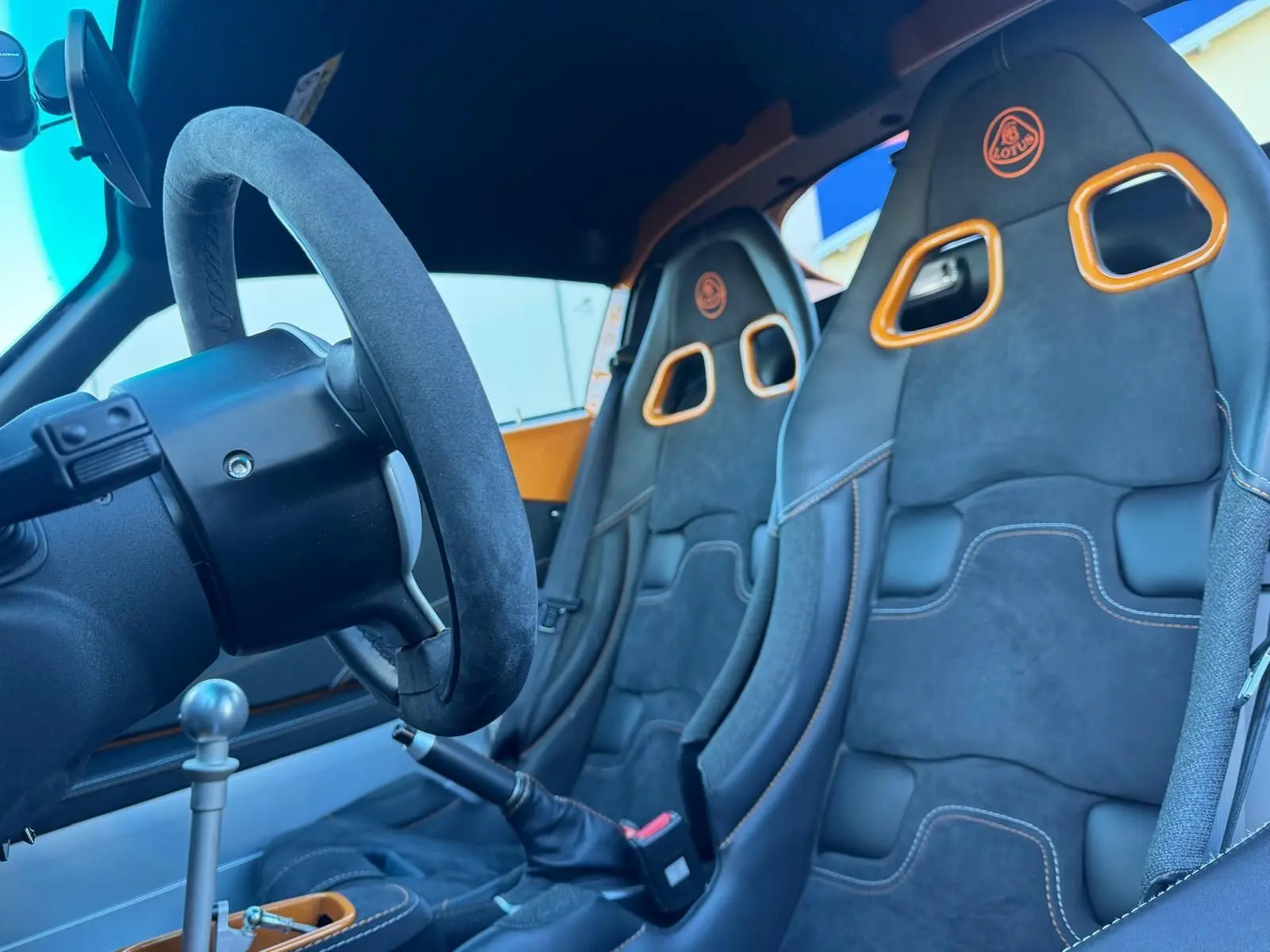 Vue intérieure côté conducteur de la Lotus Elise 3 Cup 250 2021, sièges sport noirs avec surpiqûres orange et volant cuir.