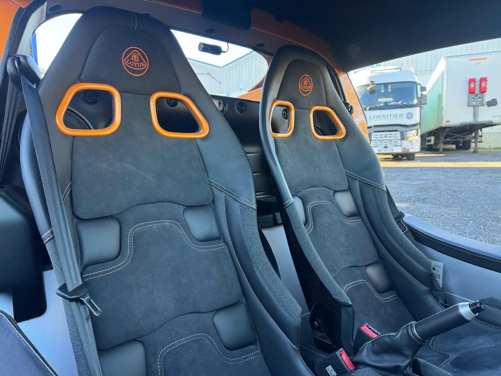 Vue intérieure rapprochée des sièges sport noirs avec surpiqûres orange et harnais de la Lotus Elise 3 Cup 250 2021.