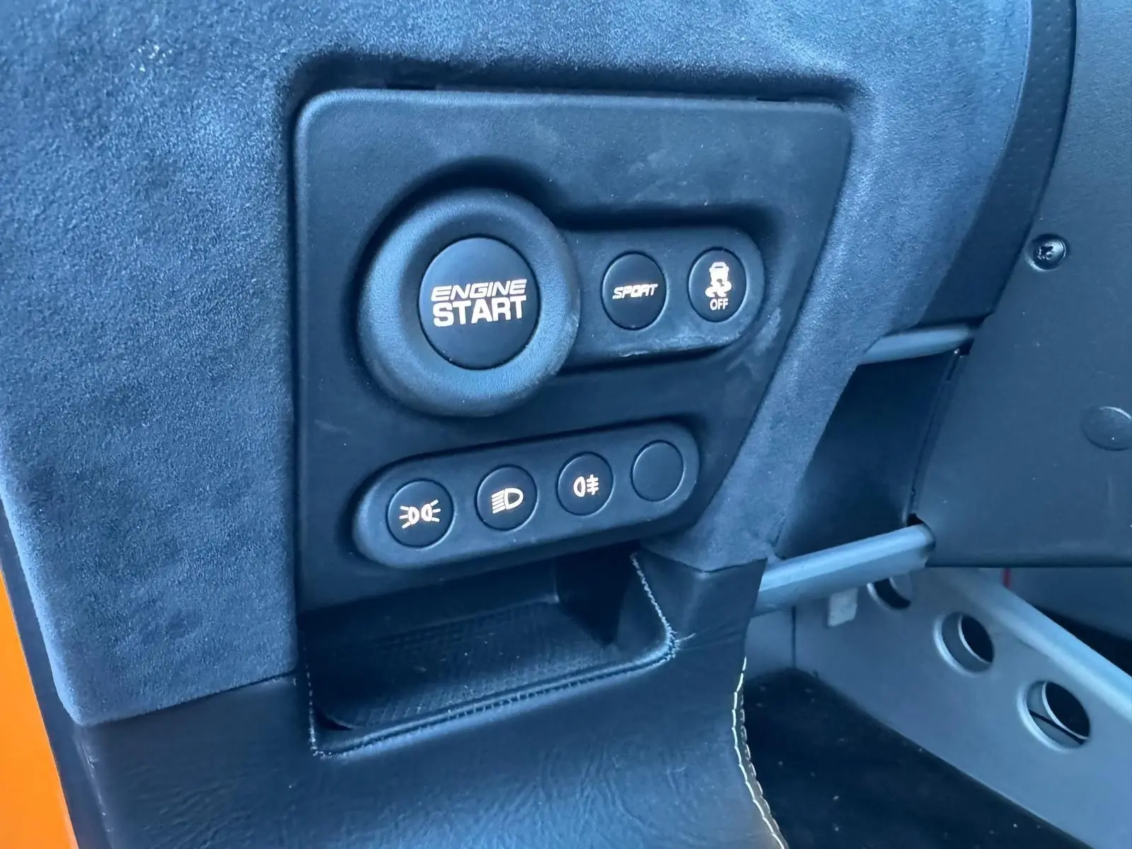 Gros plan sur le tableau de bord côté conducteur de la Lotus Elise 3 Cup 250 orange, avec bouton démarrage moteur et commandes.