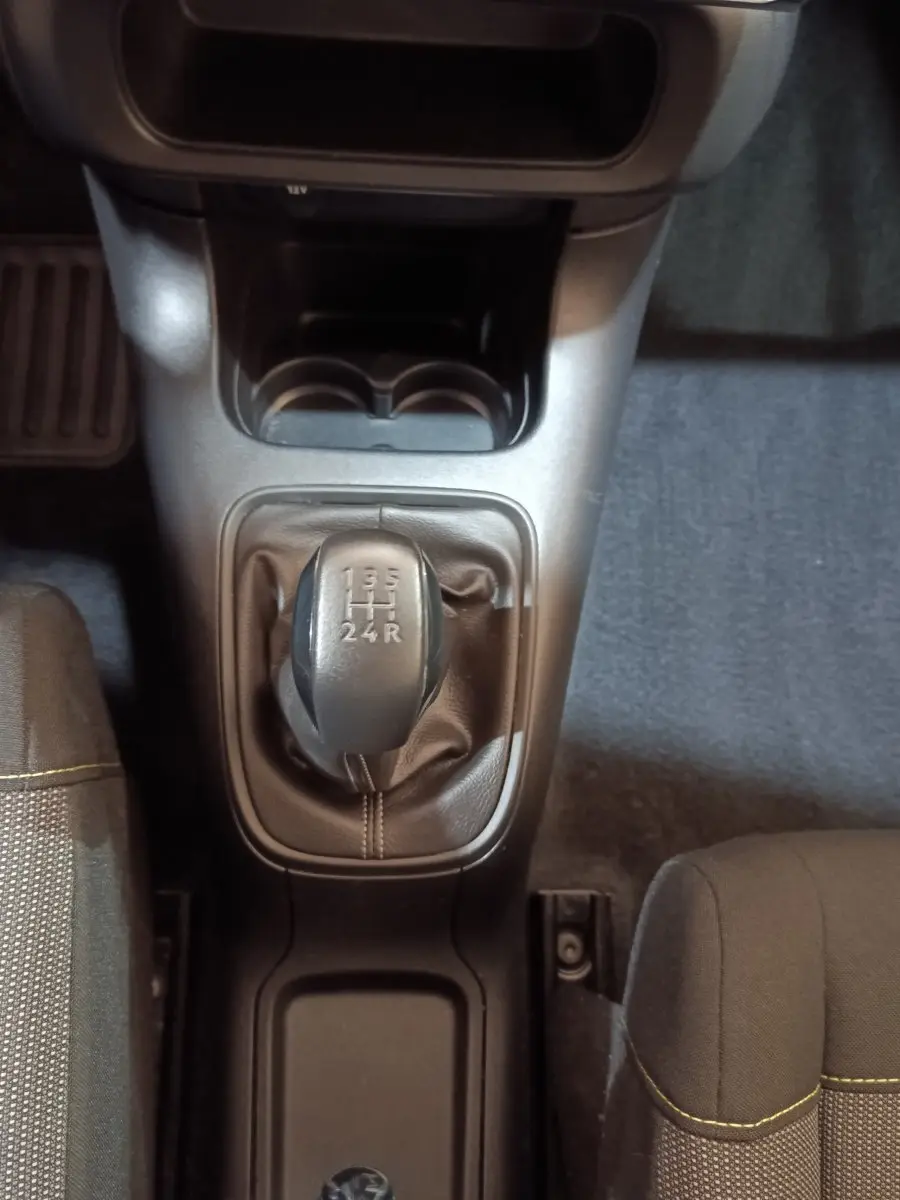 Vue plongeante sur la boîte manuelle noire de la Citroën C3 blanche, avec sièges tissu gris et surpiqûres jaunes visibles.