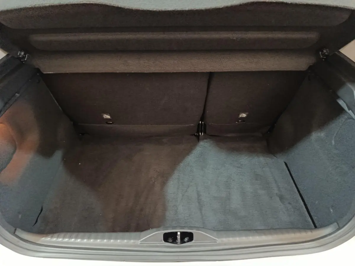 Coffre ouvert vu de l'arrière d'une Citroën C3 blanche, montrant un espace de chargement vide et tapis noir.