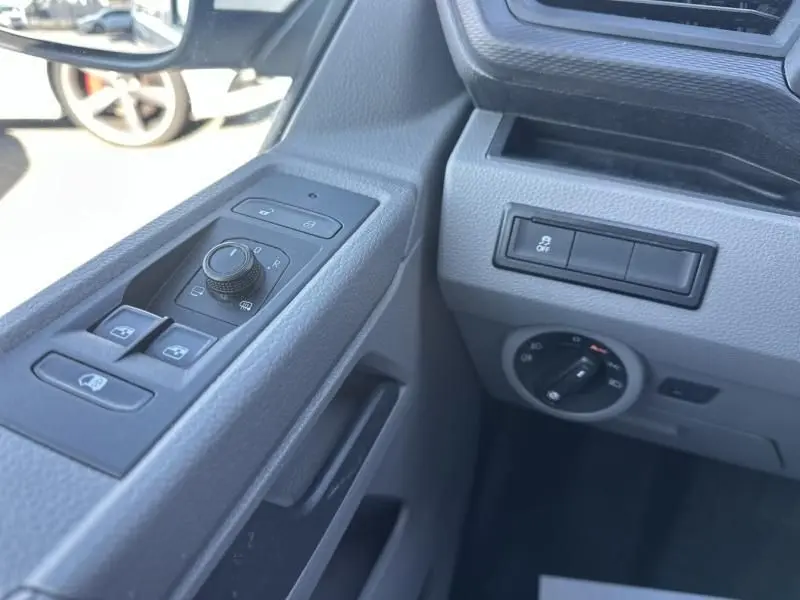 Détail intérieur côté conducteur du Volkswagen Transporter blanc 2022, montrant les commandes des vitres et des rétroviseurs.