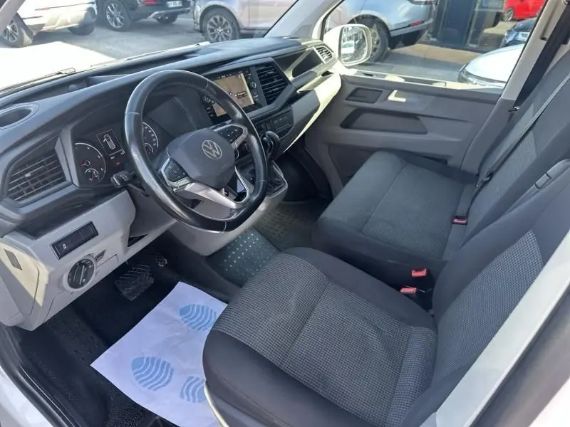 Intérieur côté conducteur du Volkswagen Transporter blanc 2022, tableau de bord moderne avec volant multifonction et sièges tissu gris.