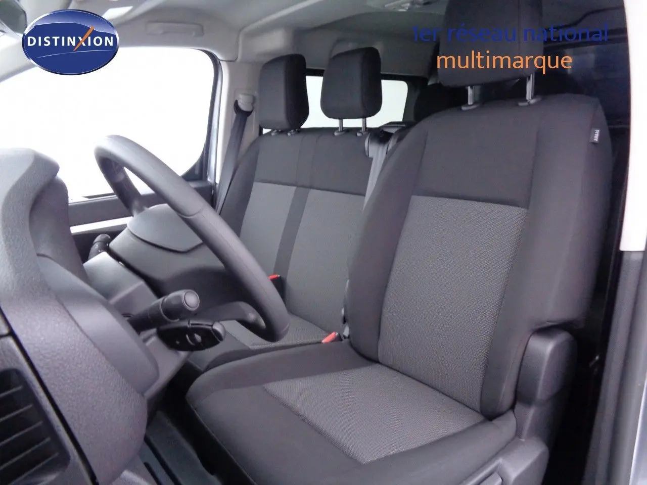 Vue intérieure côté conducteur du Peugeot Expert Long 2023, sièges noirs en tissu et volant visible.