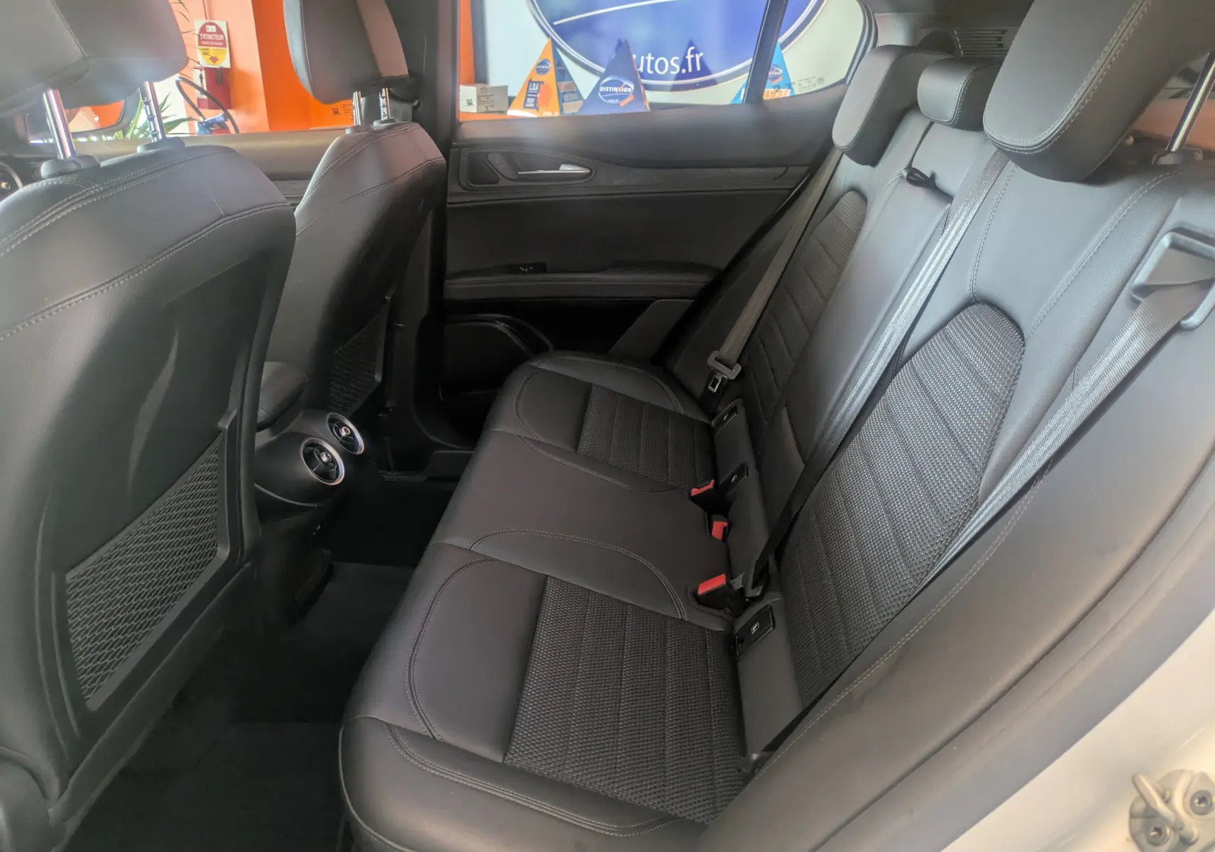 Vue intérieure côté droit des sièges arrière en cuir noir de l'Alfa Romeo Stelvio blanc 2023, avec aérateurs centraux visibles.