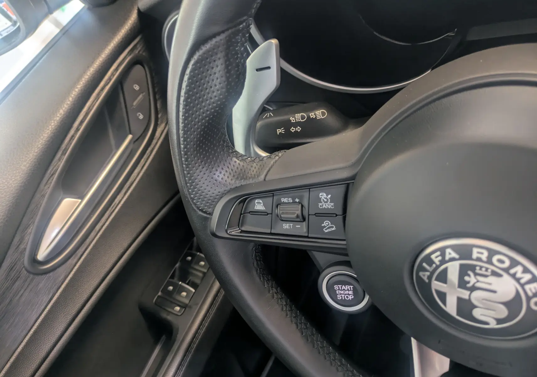 Gros plan sur le volant cuir noir de l'Alfa Romeo Stelvio blanc 2023 avec commandes au volant et bouton start/stop.