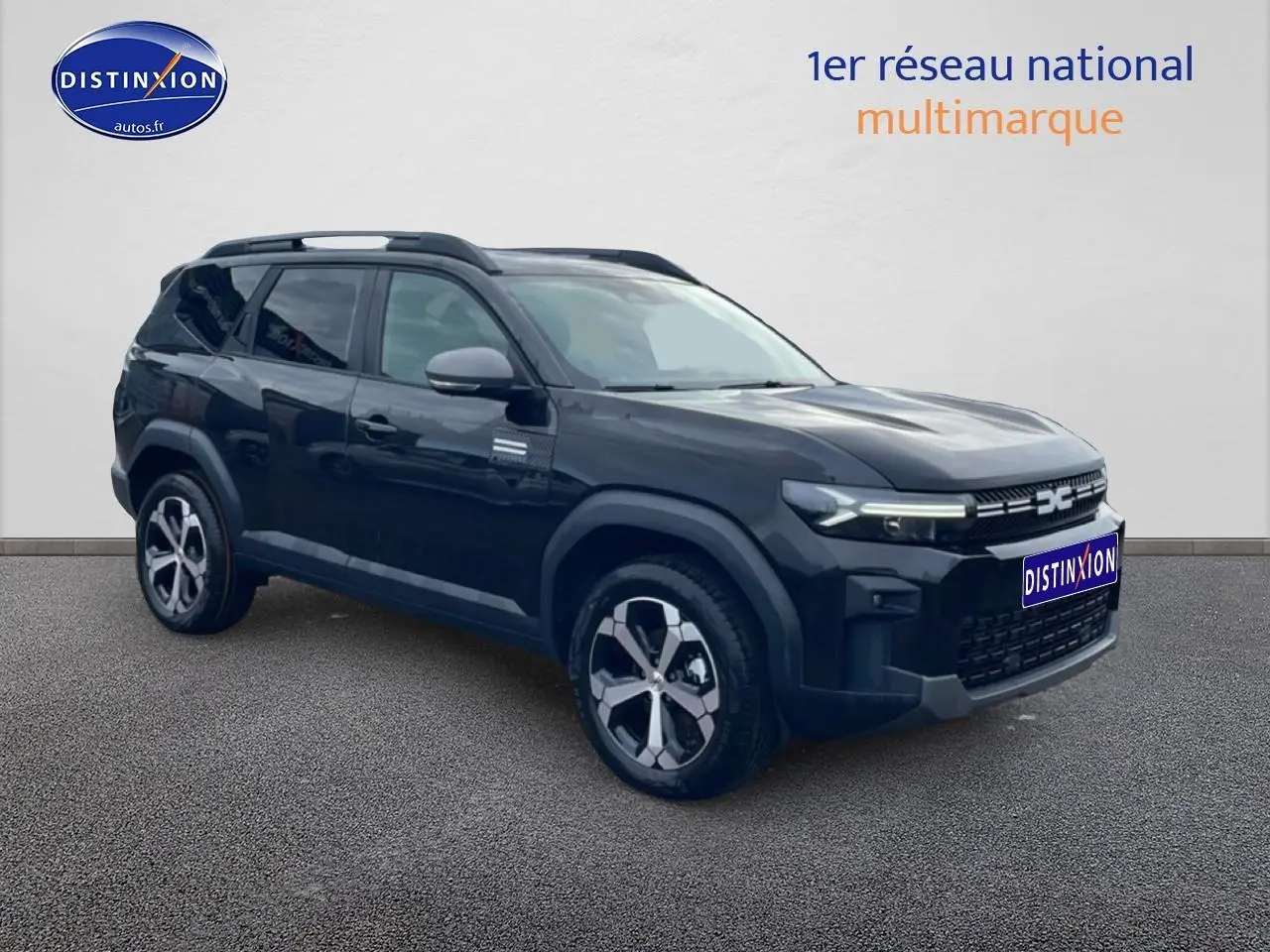 SUV Dacia Bigster noir en 3/4 avant droit avec jantes alliage diamantées et barres de toit visibles.