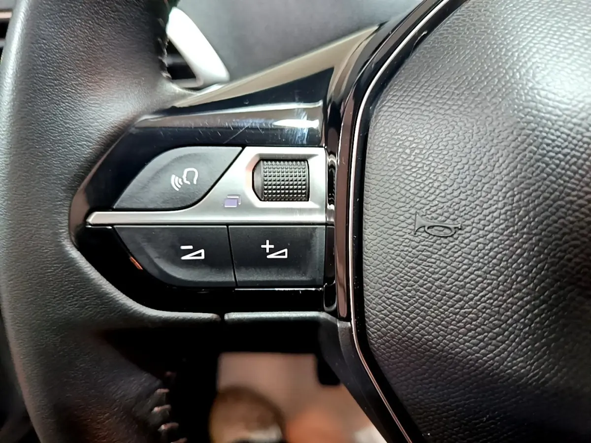 Gros plan sur les commandes gauche du volant cuir noir du Peugeot 3008 gris clair, avec boutons de volume et commande vocale.