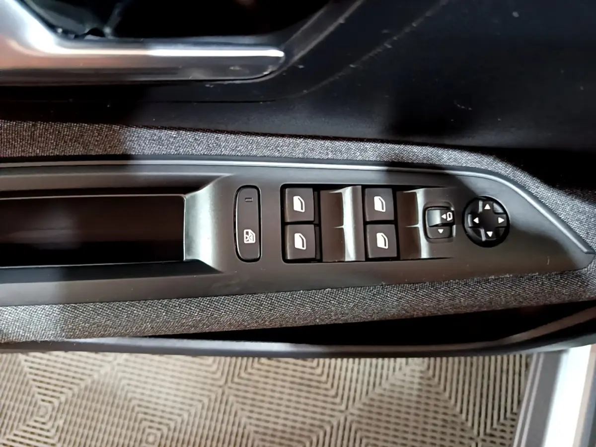 Vue rapprochée des commandes de lève-vitres et rétroviseurs sur la porte côté conducteur du Peugeot 3008 gris clair.