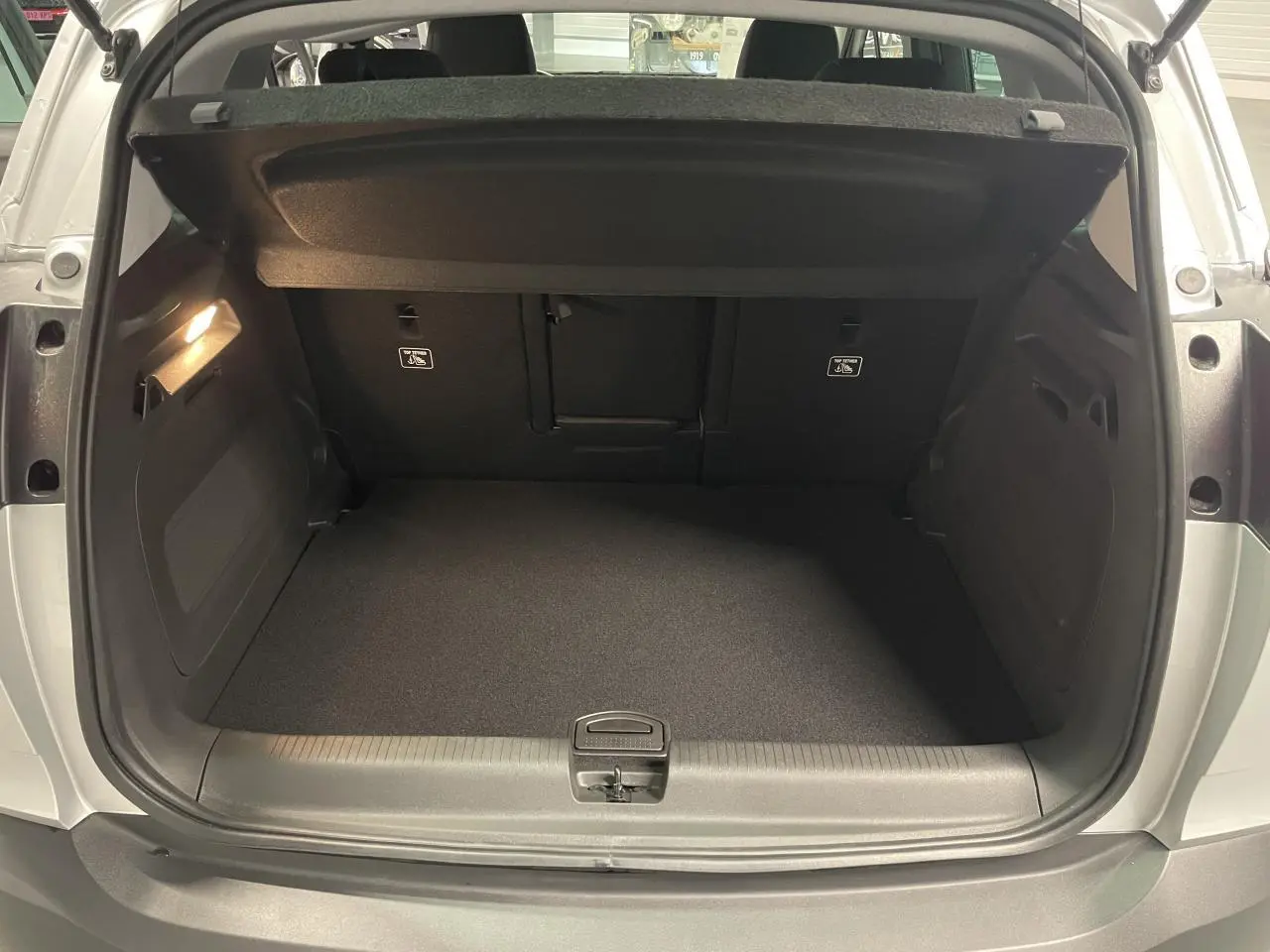 Coffre ouvert vu de l'arrière d'un Opel Crossland gris clair, montrant un espace de chargement propre et vide.