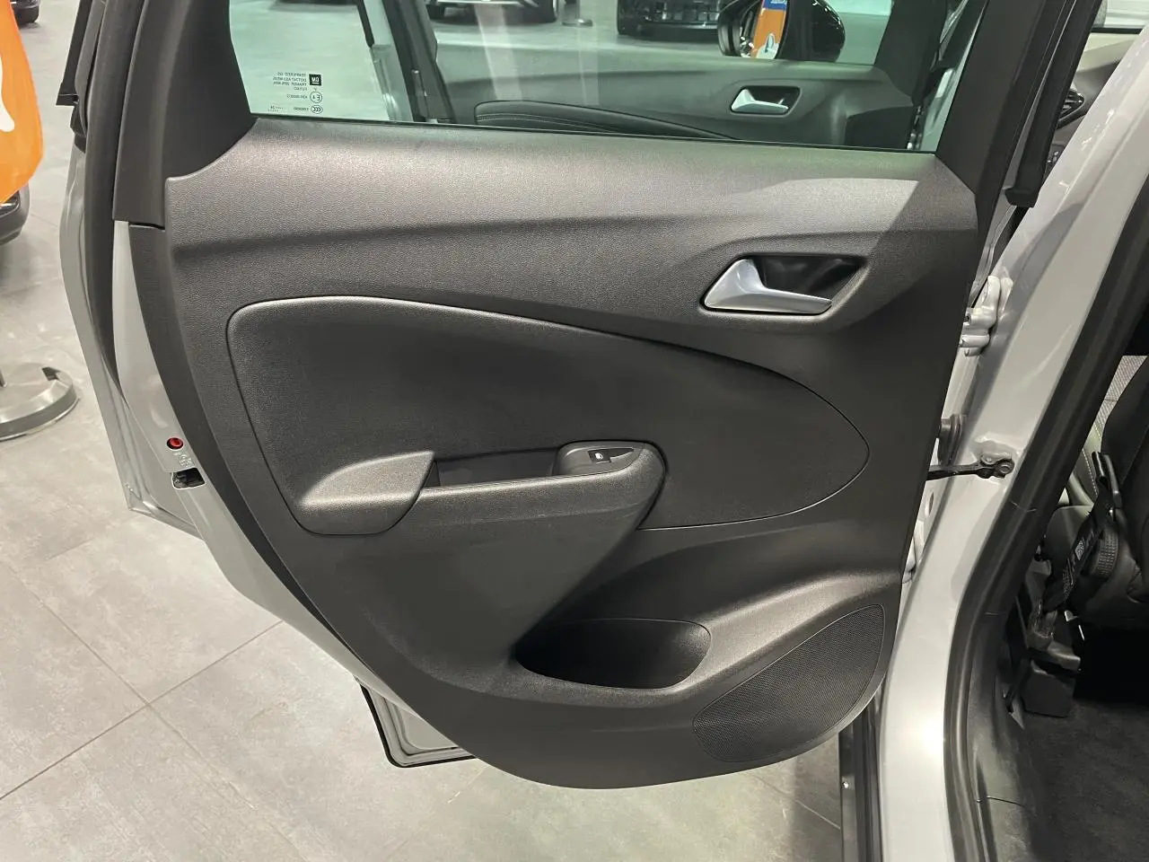 Porte arrière droite ouverte de l’Opel Crossland gris clair, montrant la garniture intérieure noire avec poignée et commande de vitre.