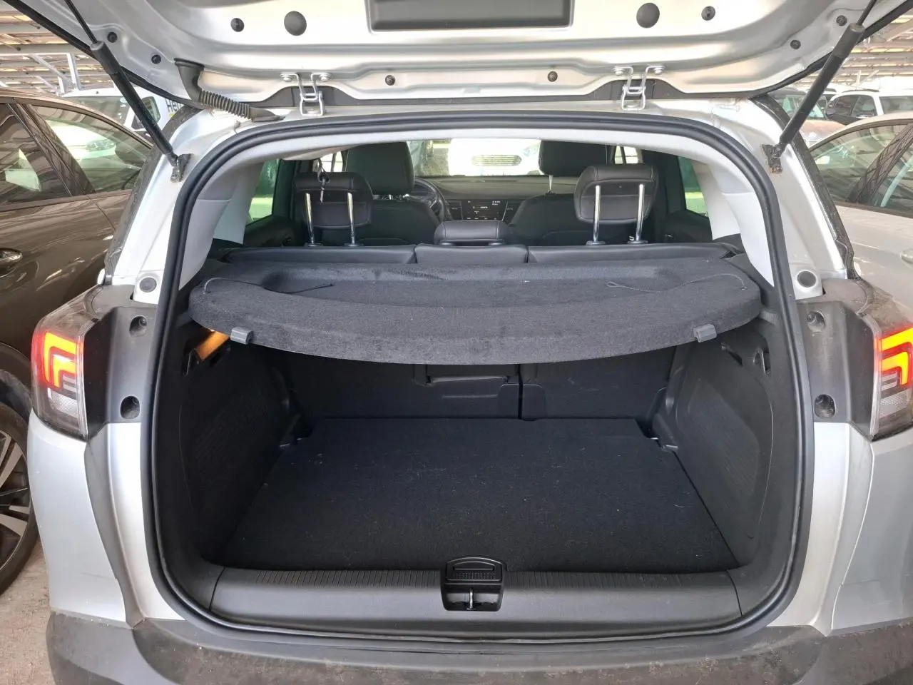 Coffre ouvert d’un Opel Crossland gris clair 2024, vue arrière montrant l’espace de chargement et la tablette cache-bagages.