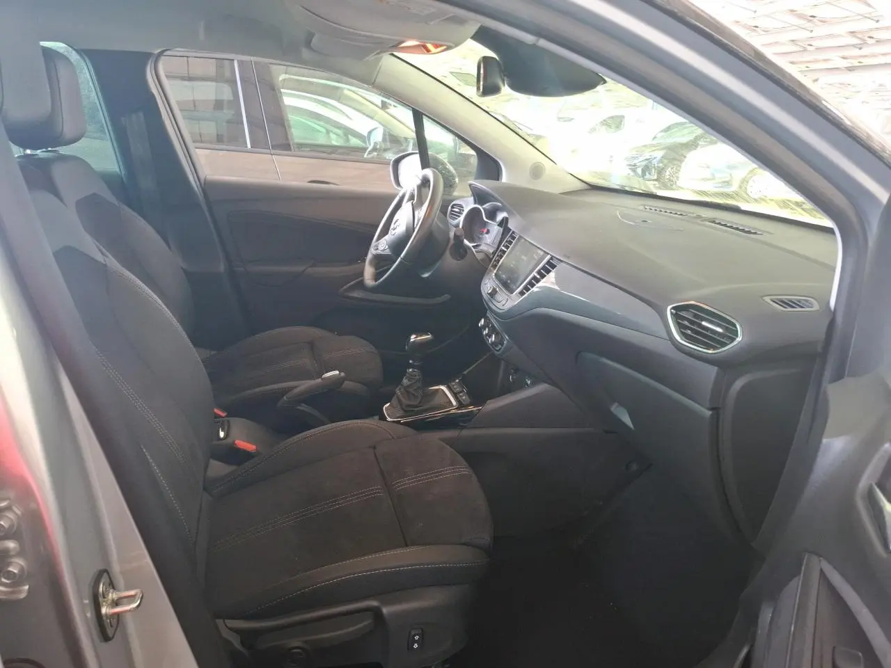 Vue intérieure côté conducteur de l'Opel Crossland gris clair 2024, avec sièges noirs et boîte manuelle visible.