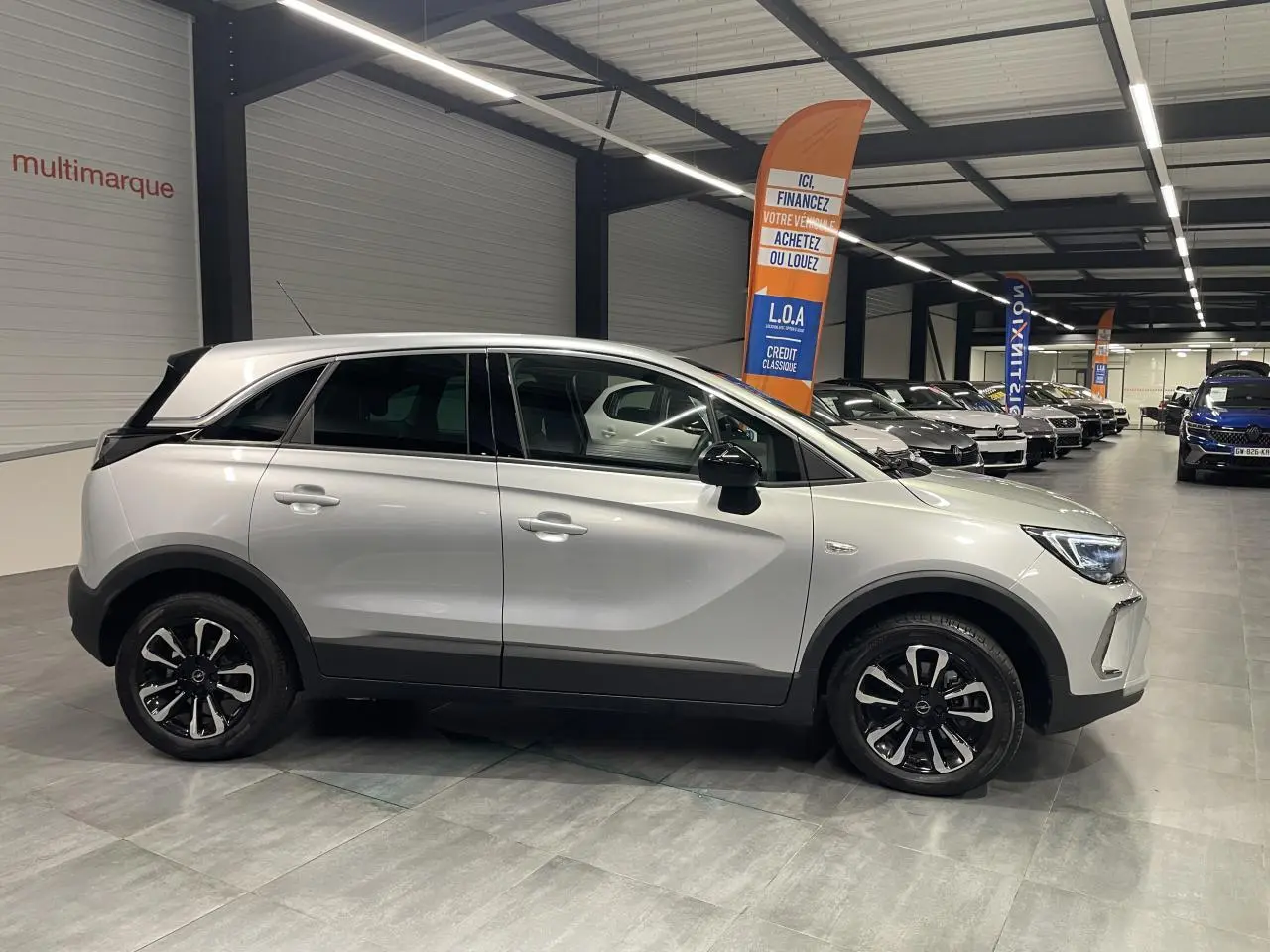 Vue de profil côté gauche d'un Opel Crossland gris clair avec jantes alliage diamantées en showroom.