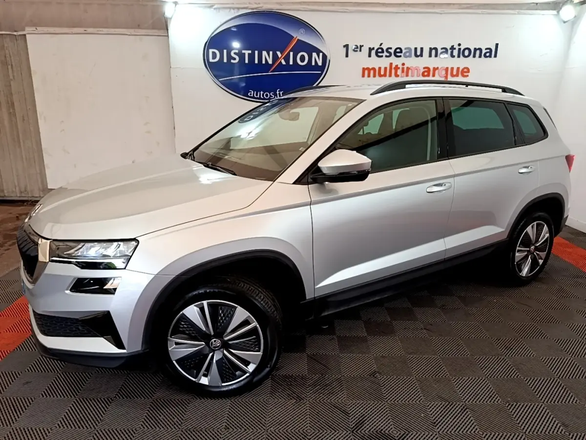Vue 3/4 avant droite d’un Skoda Karoq gris clair 2022 avec jantes alliage et barres de toit noires.