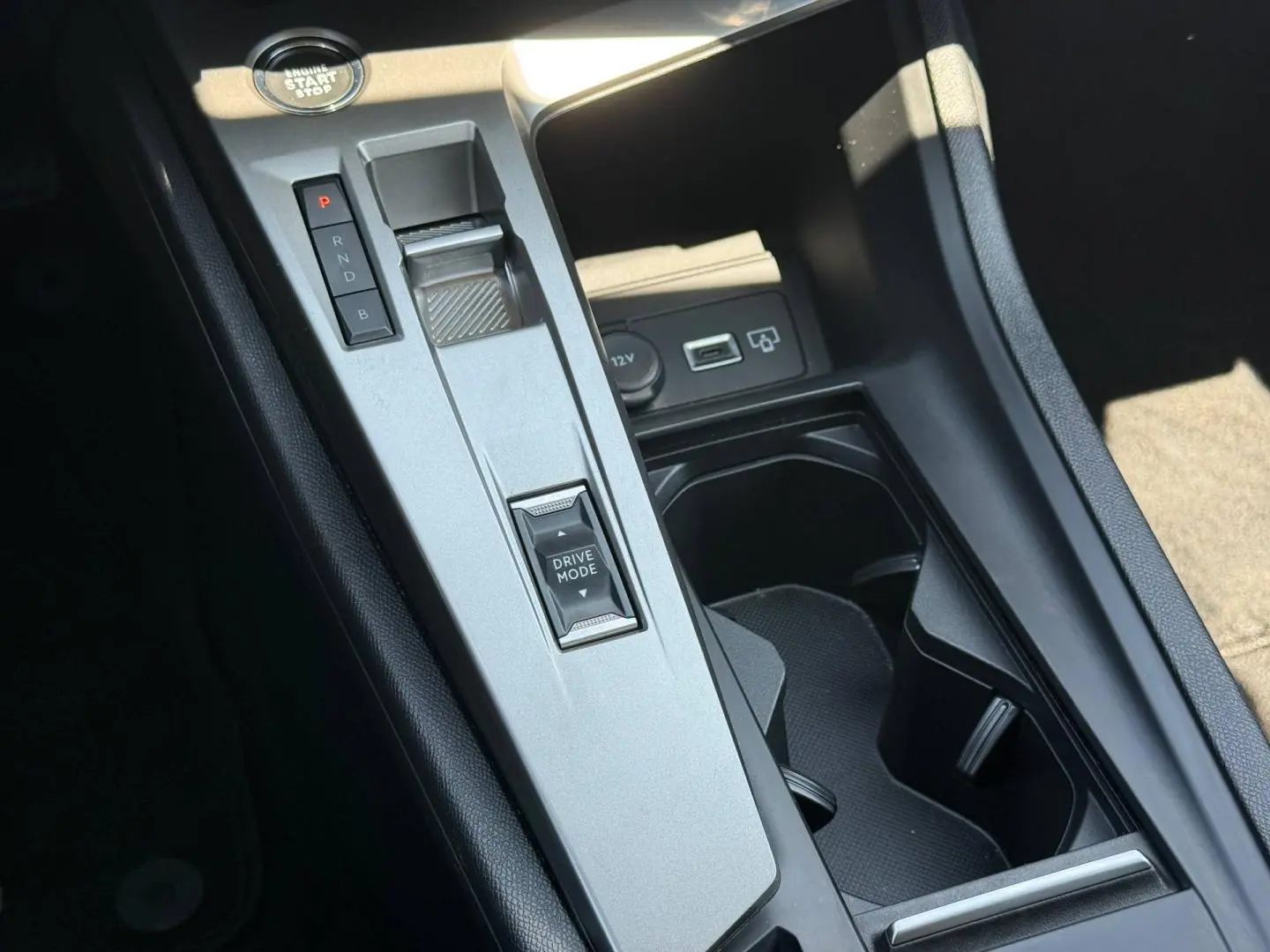 Vue rapprochée de la console centrale grise avec sélecteur de mode de conduite et bouton start/stop dans une Peugeot 308 e-308 noire.