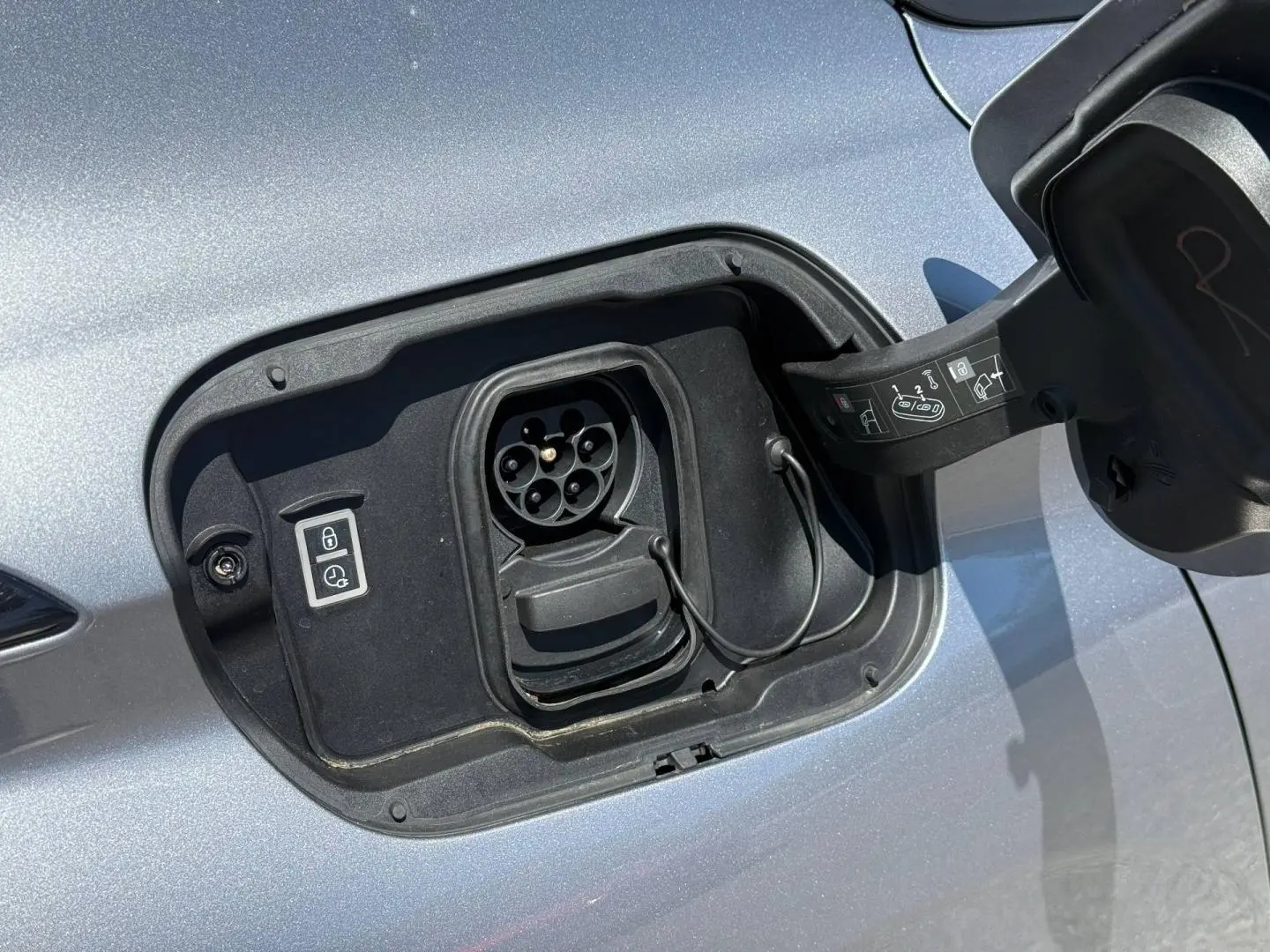 Prise de recharge électrique ouverte côté gauche sur Peugeot e-308 2025 noir Perla Nera, détail du port de charge.