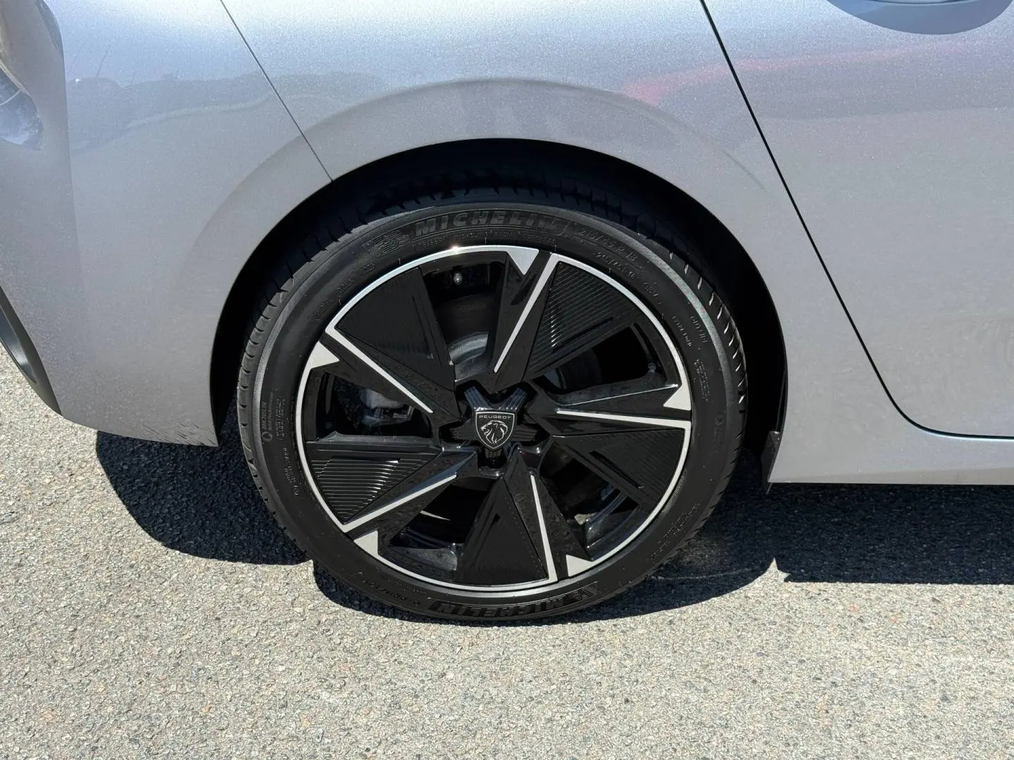Gros plan sur la roue arrière droite d'une Peugeot 308 e-308 noire avec jante alu noire et argentée au design moderne.
