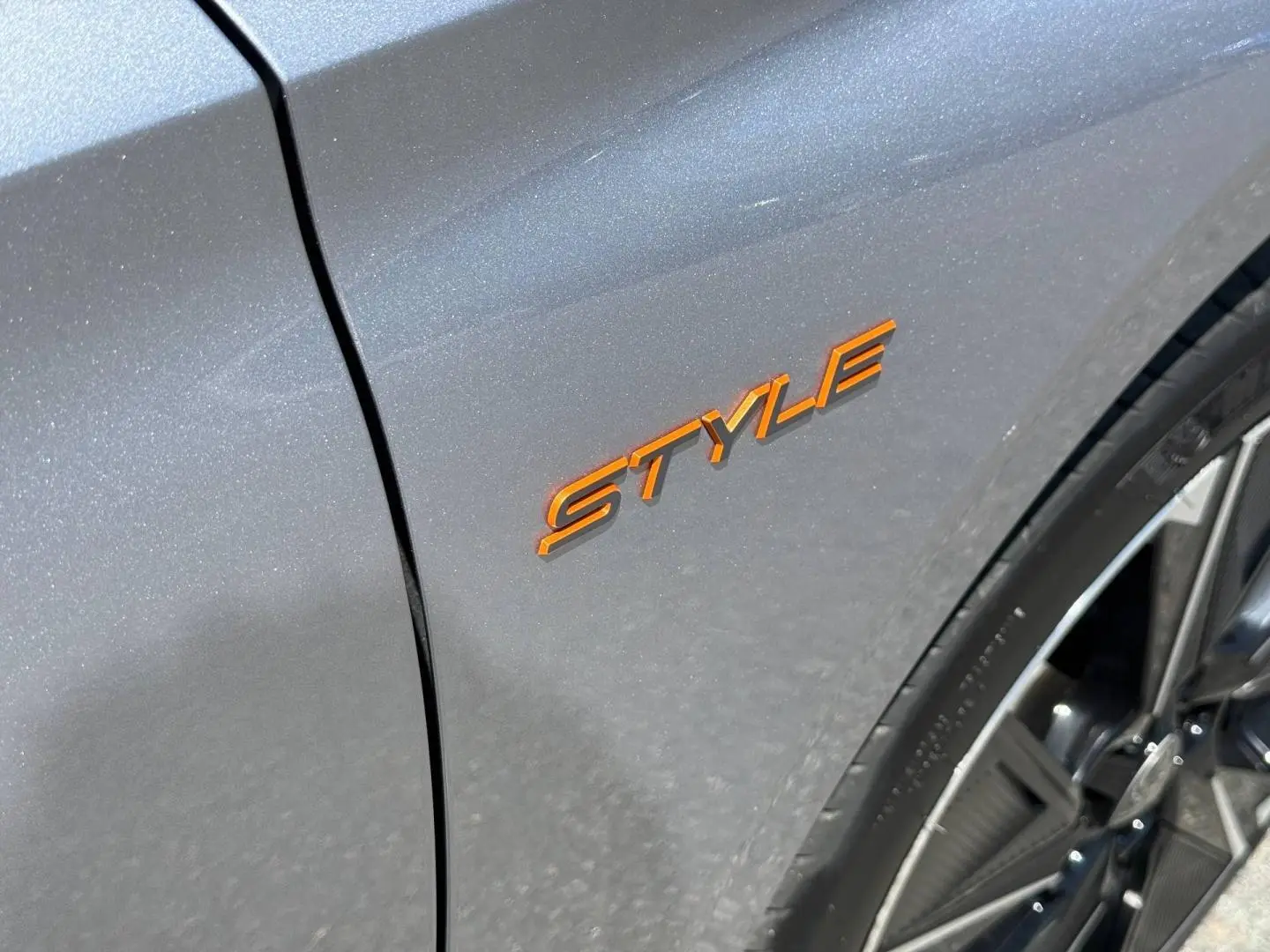 Gros plan sur l’inscription orange Style sur l’aile avant droite d’une Peugeot 308 e-308 noire avec jante alu visible.