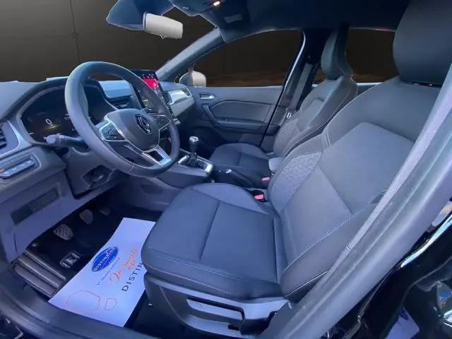 Vue intérieure côté conducteur du Renault Captur noir 2024, mettant en valeur la sellerie tissu noire et la console avec écran tactile.
